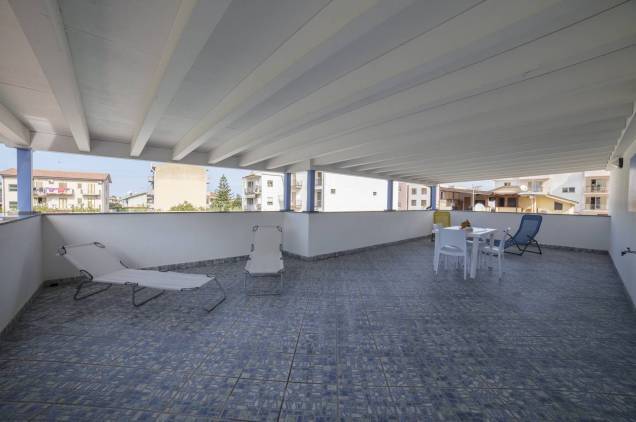 Die überdachte Terrasse mit Tischen, Stühlen und Sonnenliegen ausgestattet
